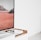 A modern interior setting featuring a white entertainment console with wooden accents. On the console, there is a gaming console with a controller on top. A large framed picture of a desert landscape with red sand and rocky formations is positioned next to the console.