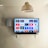 A modern living room features a wall-mounted flat-screen television displaying multiple streaming app icons, such as Apple TV, HBO Max, Netflix, Disney+, and Prime Video. Below the TV is a soundbar sitting on a small white shelf. A wicker pendant light hangs from the ceiling above, and the wall is painted a neutral color.