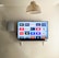 A modern living room features a wall-mounted flat-screen television displaying multiple streaming app icons, such as Apple TV, HBO Max, Netflix, Disney+, and Prime Video. Below the TV is a soundbar sitting on a small white shelf. A wicker pendant light hangs from the ceiling above, and the wall is painted a neutral color.