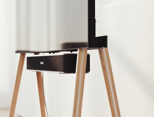 A modern television set up on sleek, angled wooden legs with a soundbar positioned directly beneath it. The design is minimalist and stylish, integrating functionality with aesthetics in a clean, contemporary space.